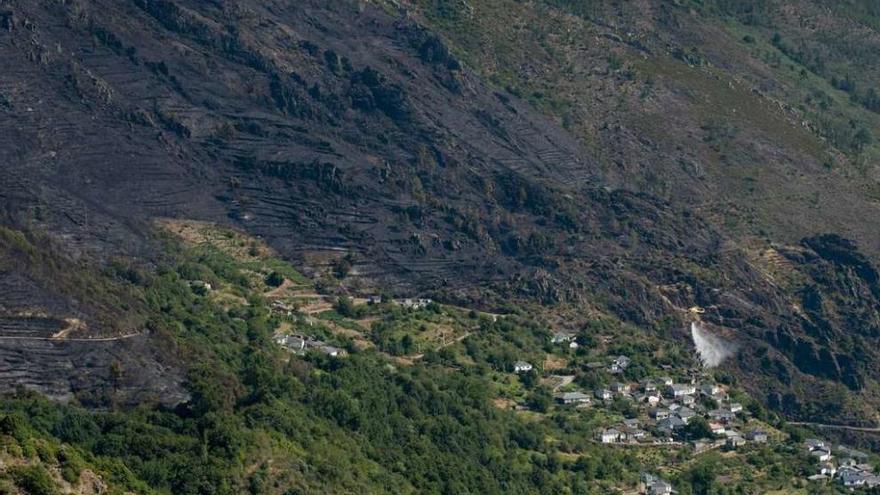 Un helicóptero suelta agua cerca de una casa, ayer en Cangas, tras un incendio forestal.