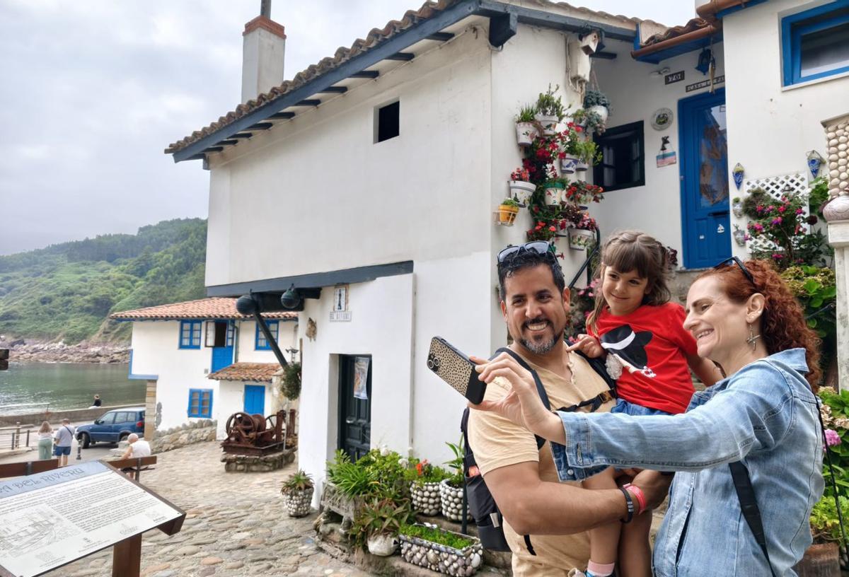 Sobre estas líneas, Montse Rebollar Varas se hace un selfi delante de su vivienda, conocida popularmente como Casa El Rivero, en el puerto de Tazones (Villaviciosa), donde se inició la moda local de decorar con conchas de moluscos las macetas y paredes de las casas cercanas al  muelle. Debajo desde la izquierda, un grupo de turistas con guía delante de Casa El Rivero y una imagen de la localidad maliayesa  tomada desde la zona del puerto, muy cerca de la sede de la histórica Cofradía de Pescadores San Miguel de Tazones.  | S. ARIAS