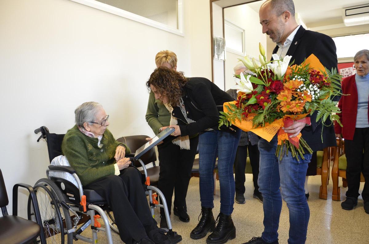 La regidora Homs i l'alcalde Aloy lliuren l'obsequi i el ram de flors a la centenària