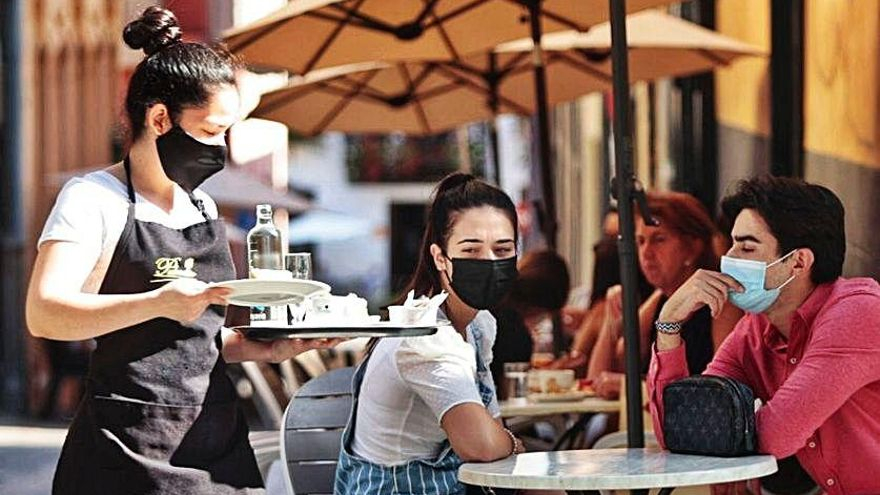 Una camarera atiende a los clientes de la terraza.