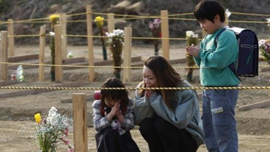 Una mujer reza, junto con sus dos hijos, ante el lugar en el que está enterrado su marido, fallecido tras el tsunami del pasado 11 de marzo.