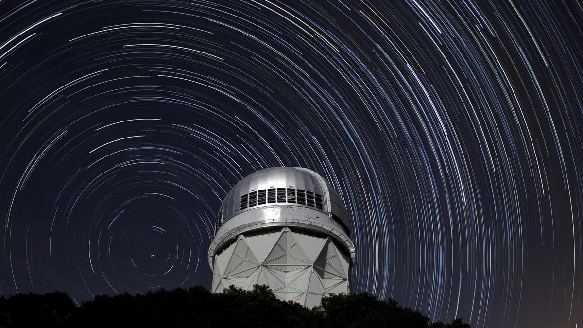 Imagen del telescopio Mayall en el Kitt Peak National Observatory, Arizona, con las sendas estelares en el fondo producidas por la rotación de la Tierra. Podría imaginarse el mismo fenómeno pero a nivel cósmico, donde el Universo girase como un tiovivo. Quizás así sería posible explicar la llamada tensión de Hubble.