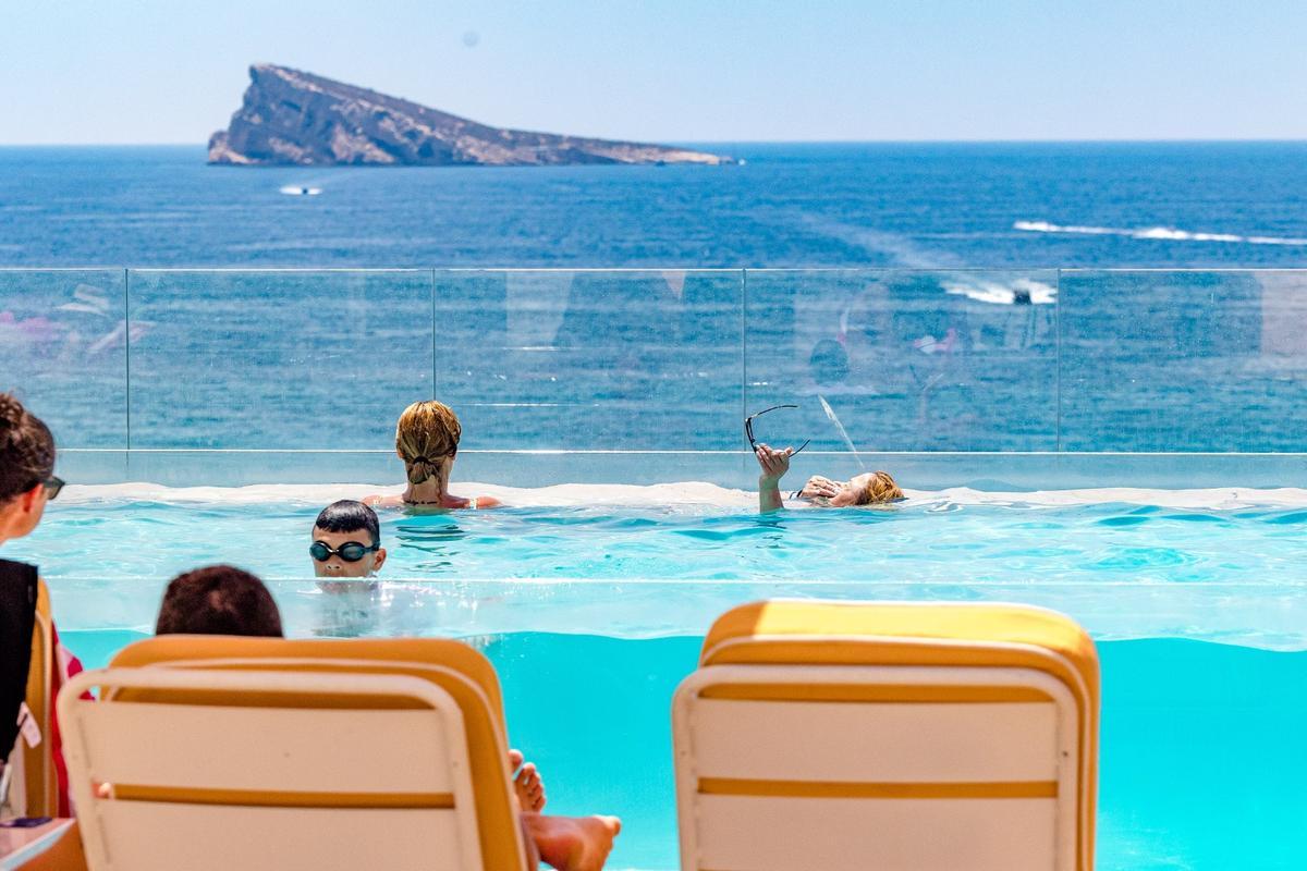 Varios turistas se bañan en la piscina de un hotel de la ciudad, con la isla al fondo.