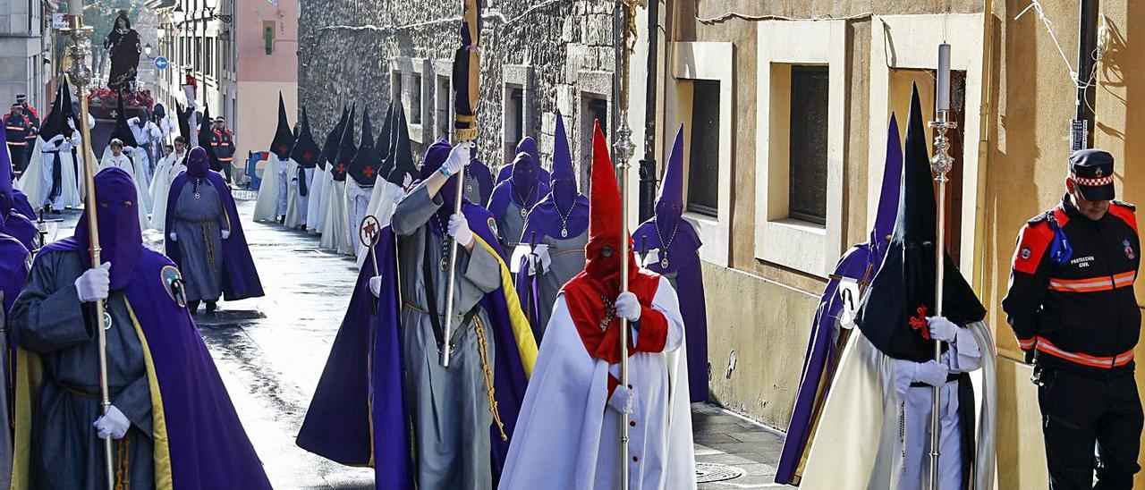 Representantes de las tres cofradías de Gijón, con la imagen de San Juan Evangelista al fondo, a su paso por la calle de Las Cruces, en Cimadevilla, en 2019.