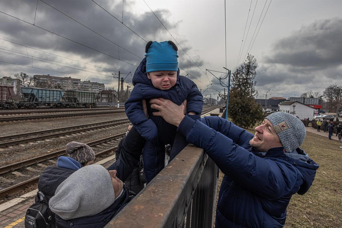 Oleg (d) pasa a su hijo Maksim por encima de una valla a su esposa Yana, antes de la llegada de un tren de evacuación a la ciudad de Kiev, en la estación de tren de Irpin, al norte del país, casi en la frontera. Mujeres y niños huyen de Bucha e Irpin, ciudades de primera línea de combates entre las fuerzas ucranianas y rusas.