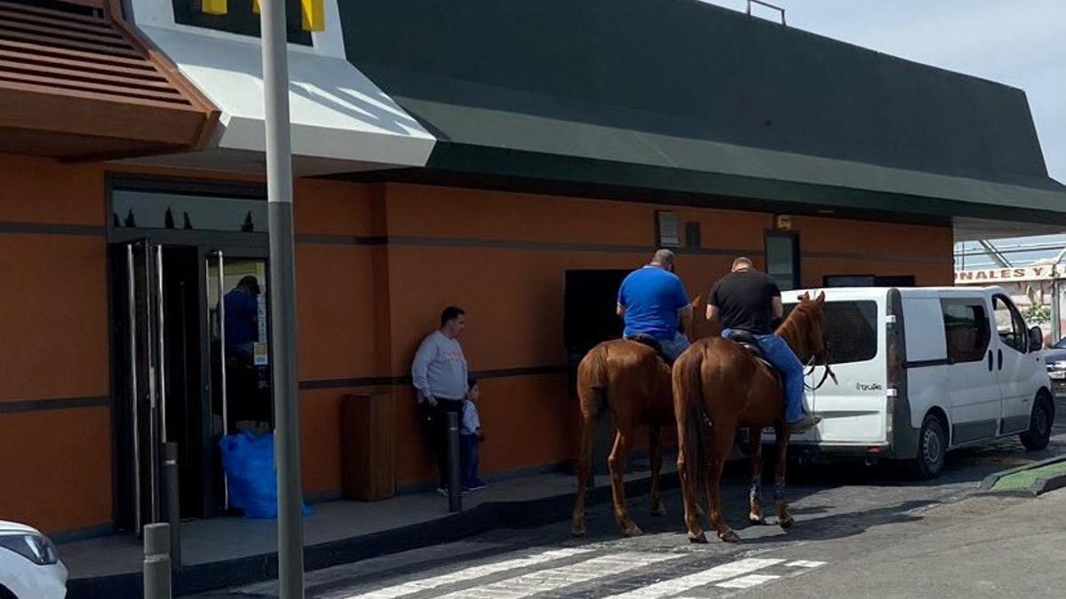 Dos hombres aguardan su turno a caballo en la cola de un McDonald de Molina.