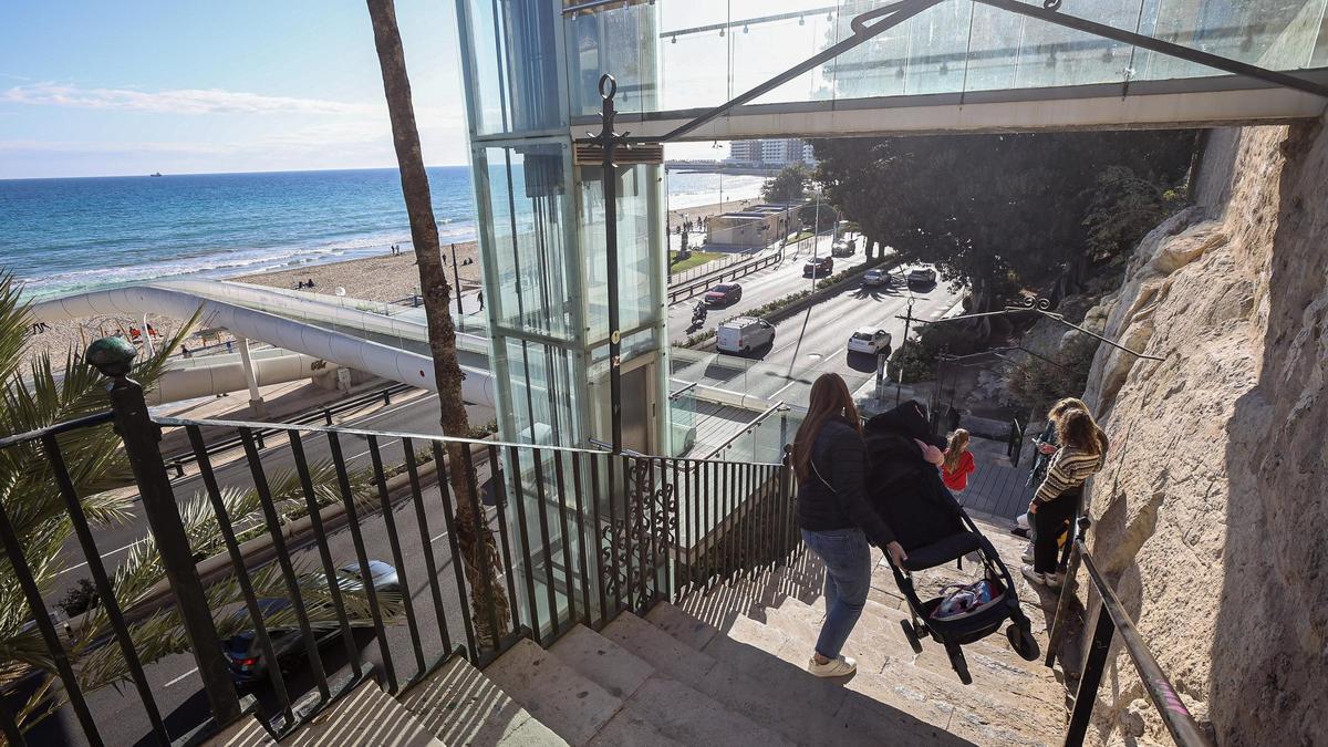 Una mujer baja a pulso un carrito de bebé por las escaleras del Raval Roig al no funcionar el ascensor, este lunes