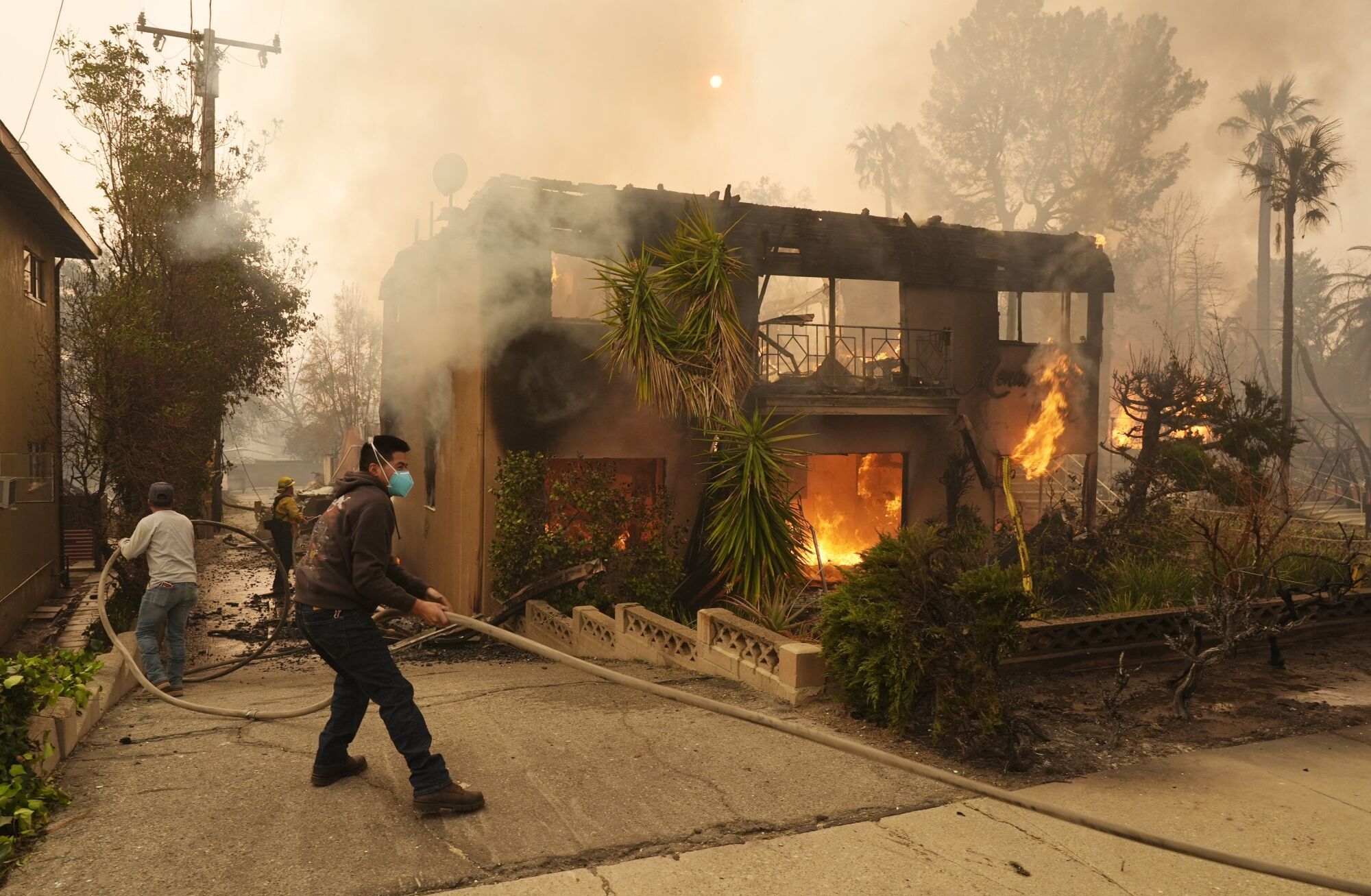 Pedestrians help a firefighter stretch a hose as an apartment building burns, Wednesday, Jan. 8, 2025, in the Altadena section of Pasadena, Calif. (AP Photo/Chris Pizzello) Associated Press / LaPresse Only italy and Spain. EDITORIAL USE ONLY/ONLY ITALY AND SPAIN
