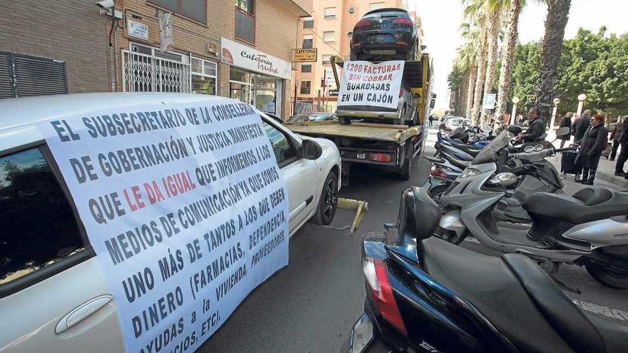 La grúa con los coches intervenidos y las pancartas de protesta por el impago de la elevada deuda.