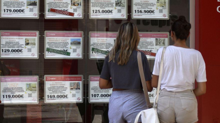 Dos jóvenes miran los precios de los pisos en el escaparate de una inmobiliaria en la capital de la Región.