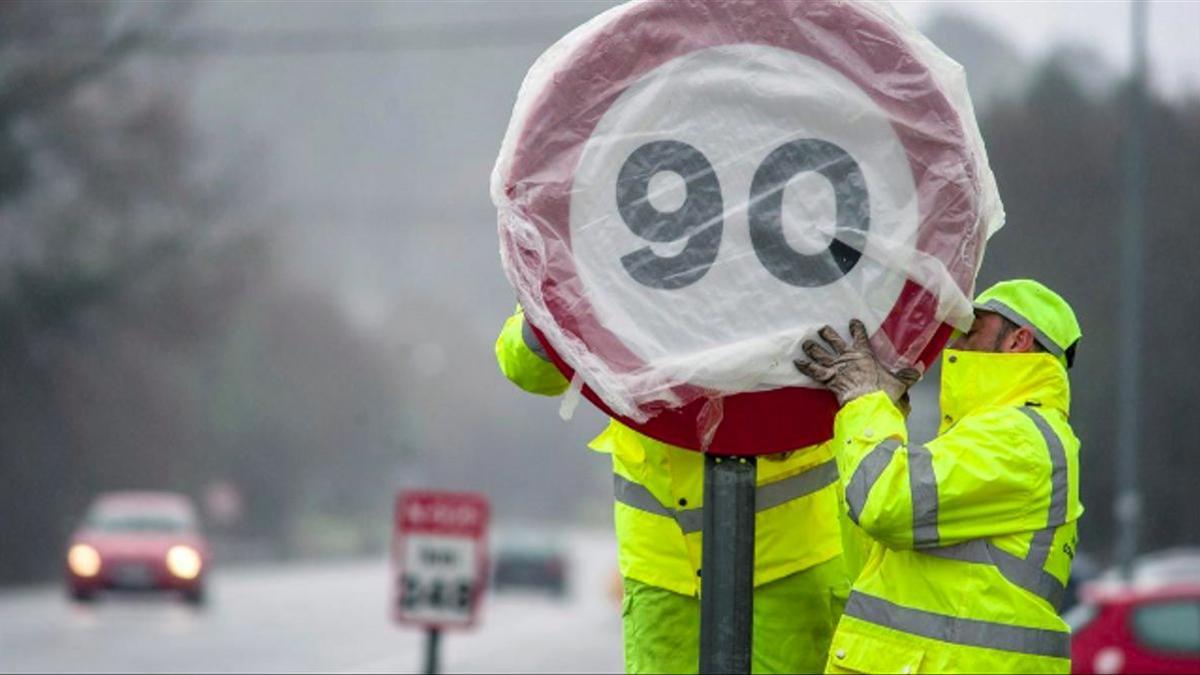 Dos operarios protegen una señal de velocidad en una carretera secundaria.