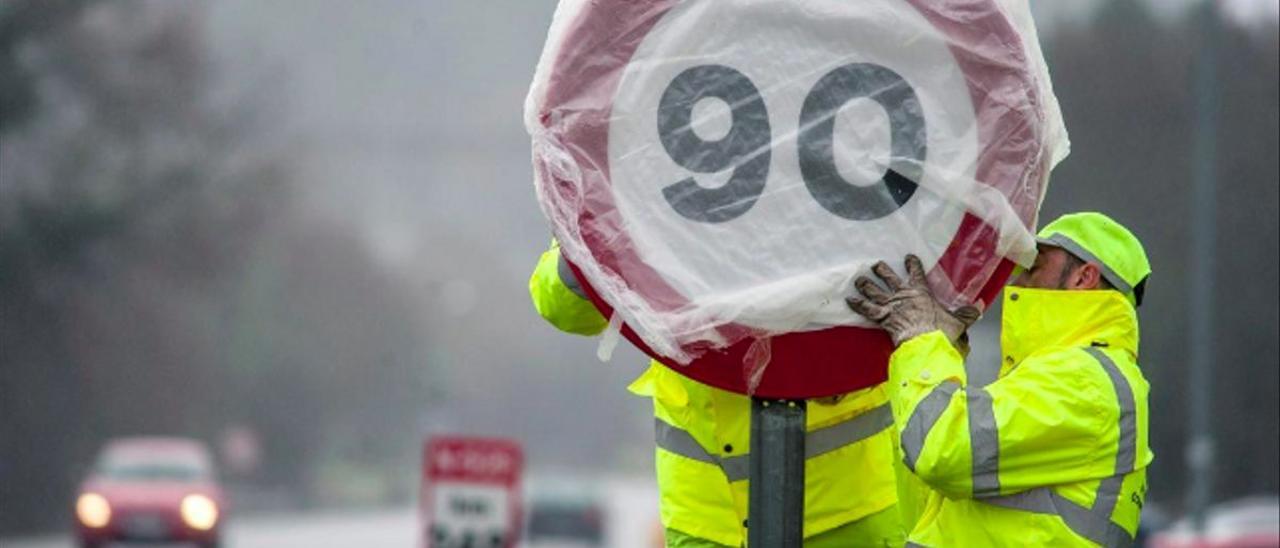 Dos operarios protegen una señal de velocidad en una carretera secundaria.