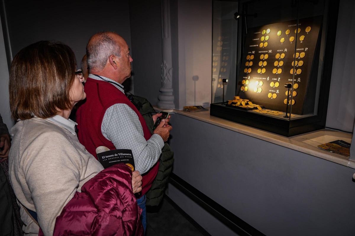 Dos extremeños observan el conjunto de las monedas expuestas en el museo de Badajoz.