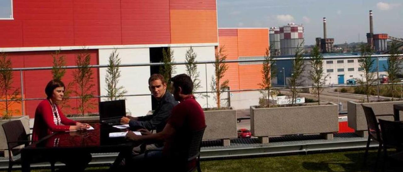 Un grupo de empleados de CSC conversa distendidamente en la terraza de su centro de trabajo con las naves de la empresa Asturfeito y las instalaciones siderúrgicas de Arcelor como telón de fondo.