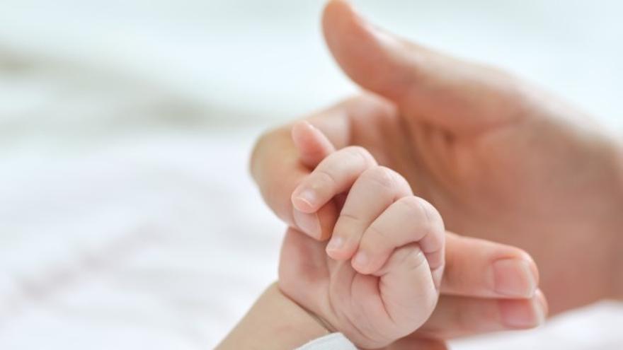 Un bebé agarra la mano de su madre.