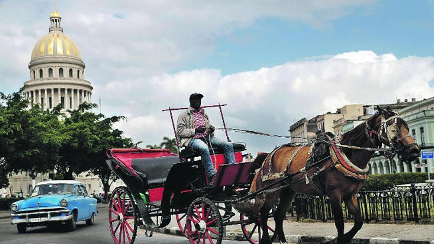 Un coche tirado por caballos y un automóvil clásico circulan por una céntrica calle de La Habana.