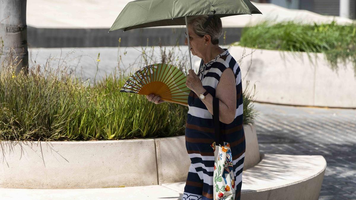 Una mujer ayer en València, protegiéndose del sol y el calor con paraguas y abanico.