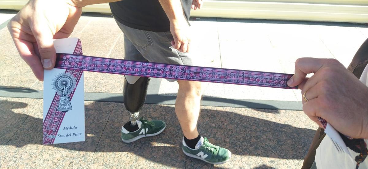 Una persona sujeta a los pies de la Basílica la nueva cinta de la medida de la Virgen del Pilar con el estampado cachirulo