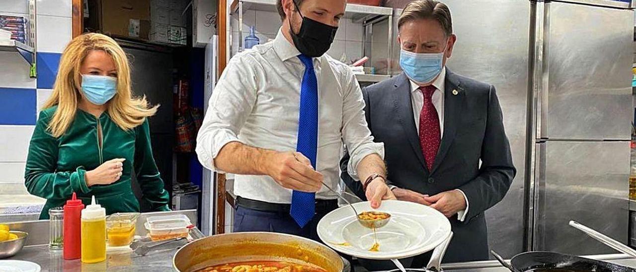 Teresa Mallada y Alfredo Canteli observan a Pablo Casado mientras sirve un plato de fabada el viernes en Oviedo.