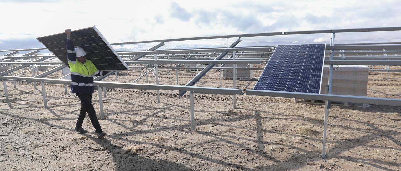 Un técnico carga con una placa solar mientras ultima la instalación de un parque fotovoltaico, en una imagen de archivo.