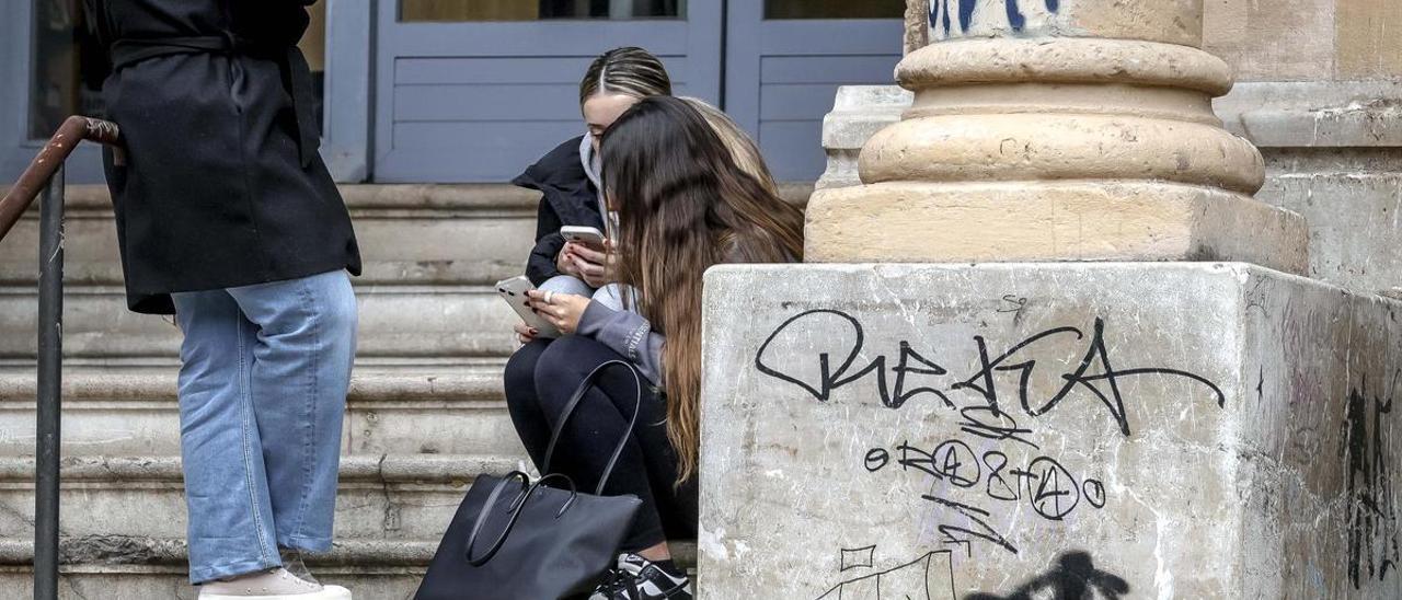 Varias jóvenes consultan  su teléfono móvil a la  salida de un instituto en Palma.