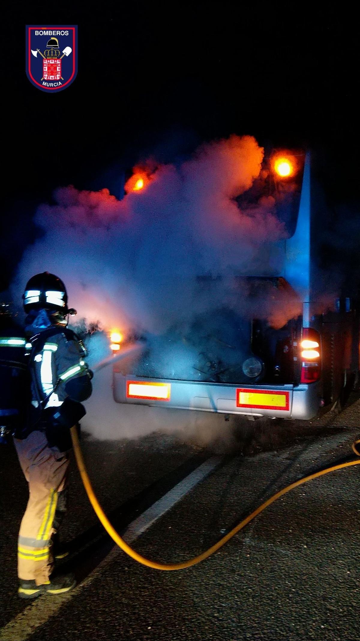 Un bombero extingue las llamas procedentes del motor del autobús.