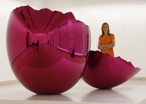 A gallery assistant poses with "Cracked Egg (Magenta)" by Jeff Koons on display at Christie's in London