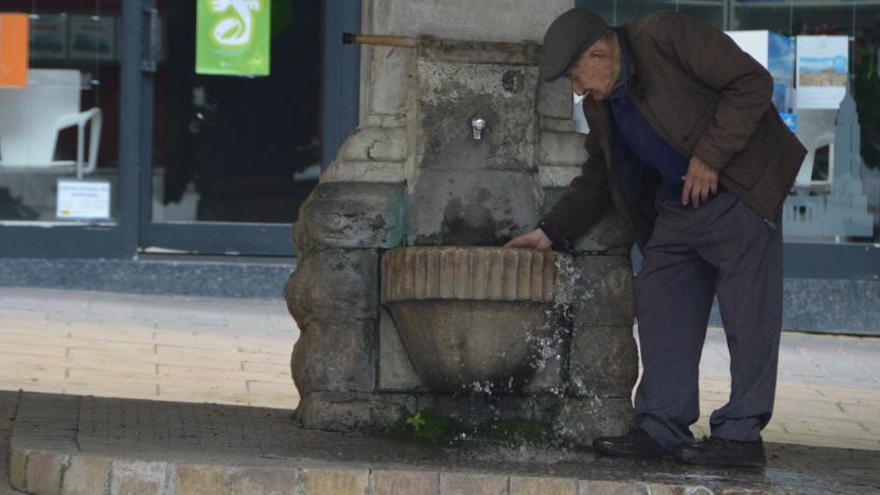 Un senyor treu aigua embassada de sota el broc de la font.