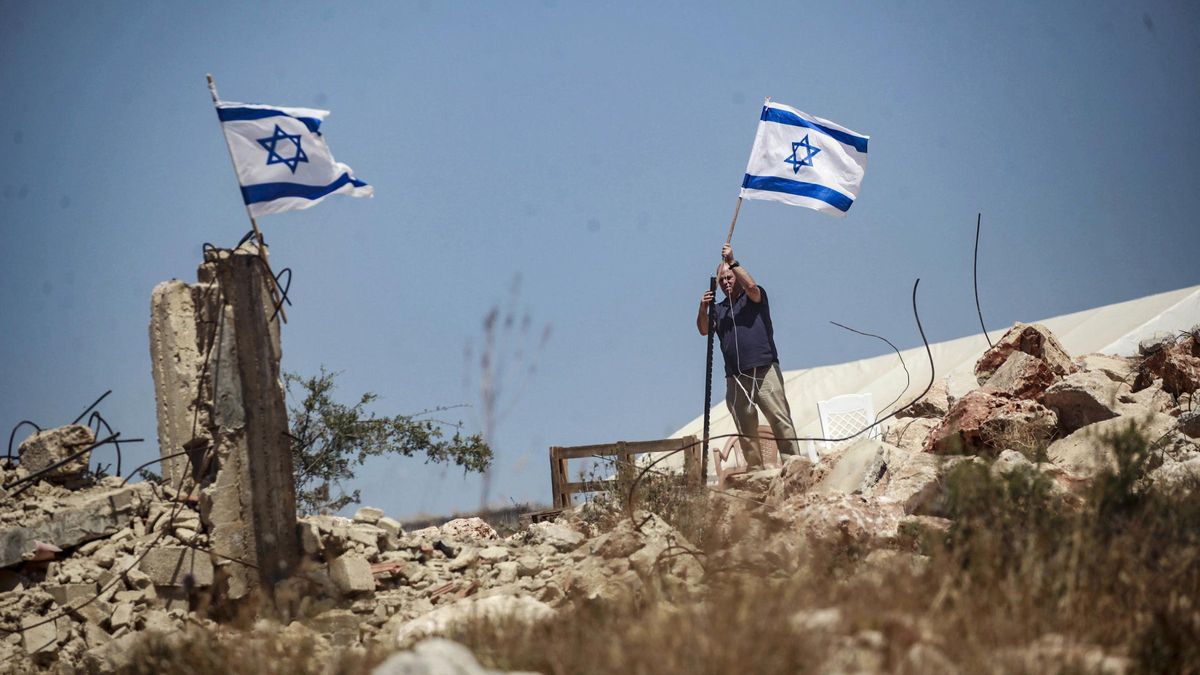 Un colono israelí iza una bandera de Israel en tierras palestinas durante un ataque a la ciudad de Bruqin, cerca de la ciudad de Salfit, en el norte de Cisjordania