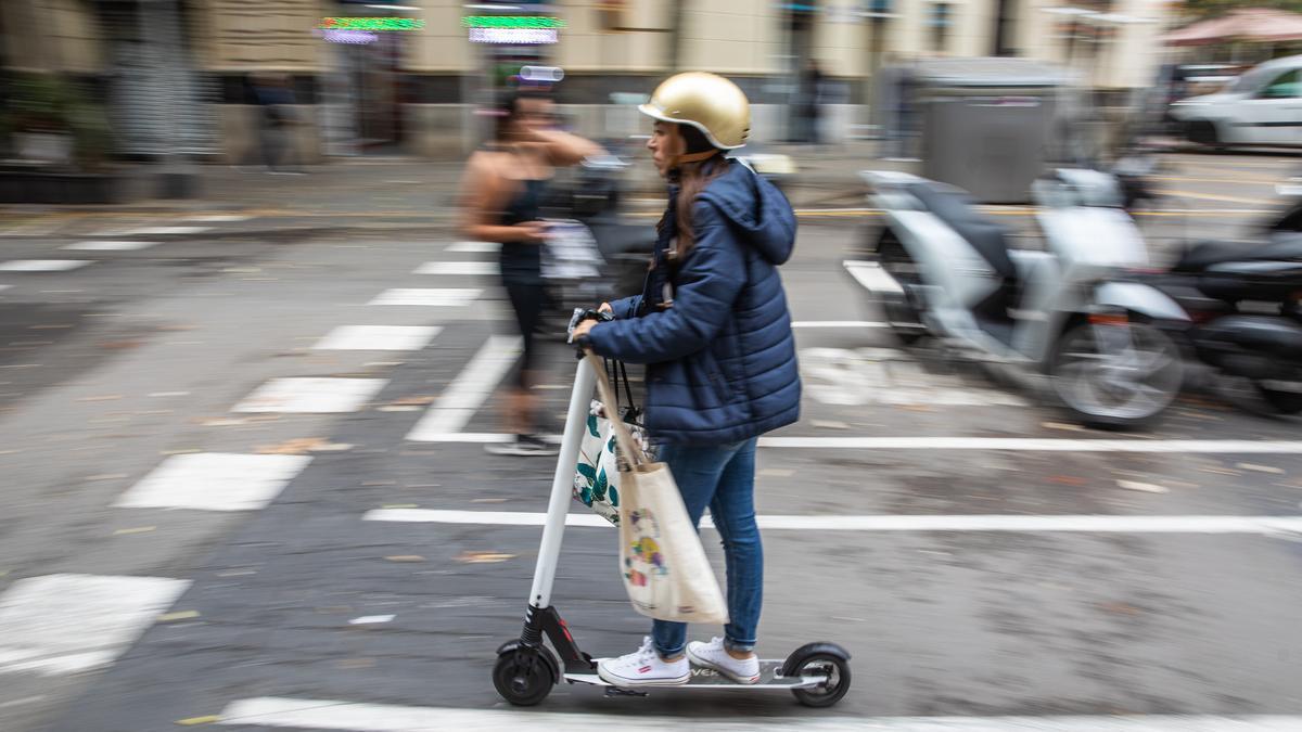 Una usuaria de patinete eléctrico, con casco, por las calles de Barcelona