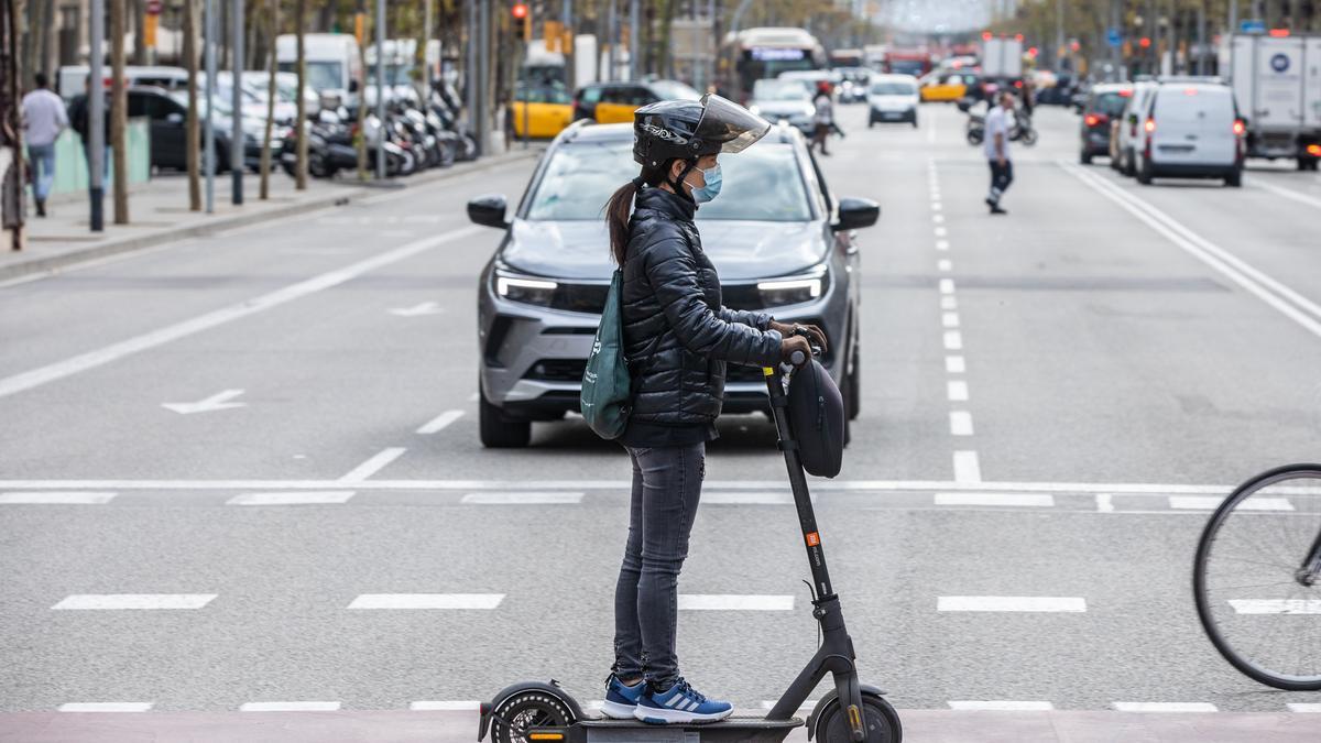 Una usuaria de patinete eléctrico, con casco, por las calles de Barcelona