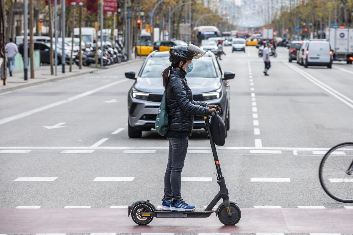Una usuaria de patinete eléctrico, con casco, por las calles de Barcelona