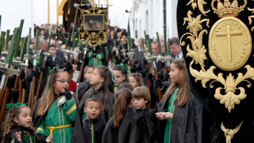 Cortejo de nazarenos de la Vera+Cruz, con los hombres de la cofradía acompañando a su titular portando hachetas.