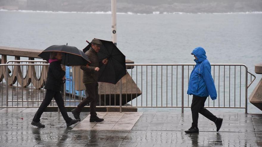 Viandantes protegidos de la lluvia con paraguas, en el paseo marítimo.