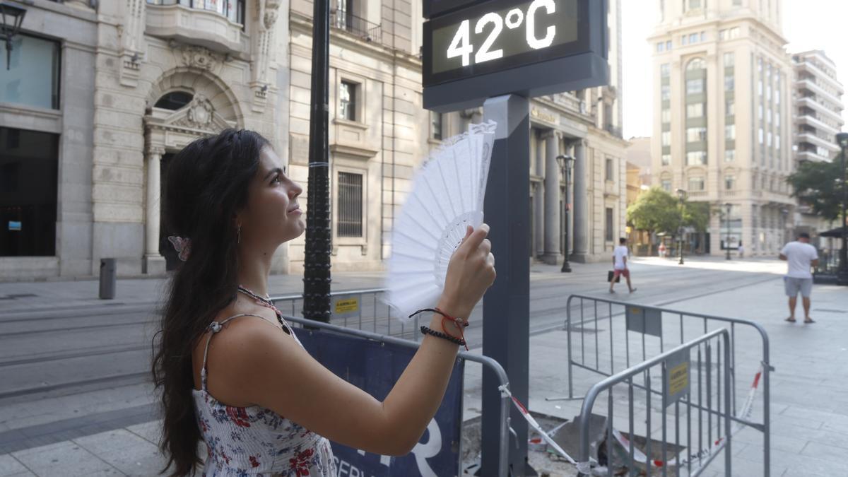 Una joven se abanica ayer en el centro de la ciudad de Zaragoza junto a un termómetro que marca una temperatura de 42 grados.