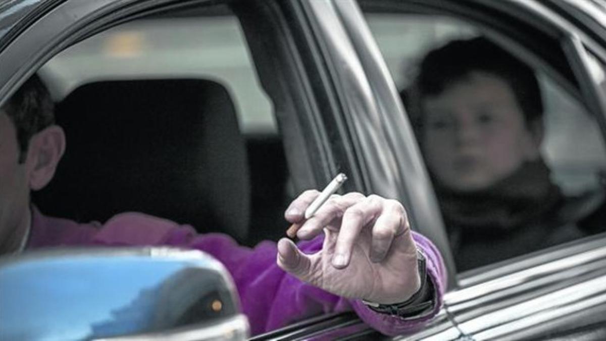 Un hombre fuma mientras conduce un coche en el que viaja con un niño.