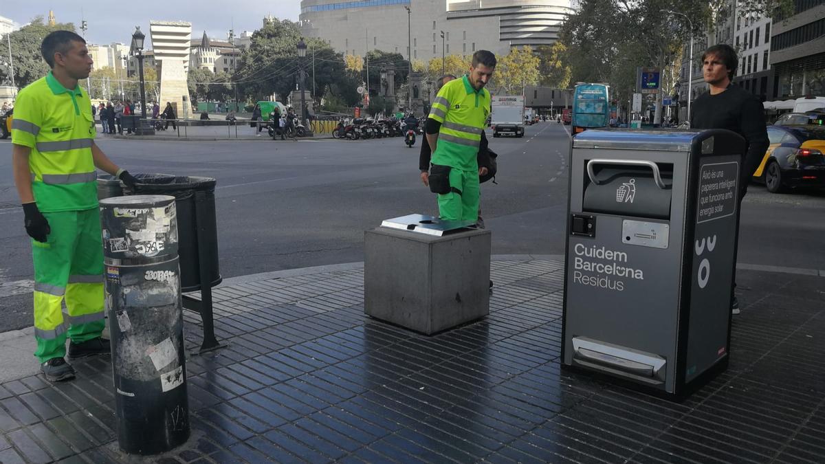 Trabajadores de la limpieza justo antes de instalarse una de las papeleras compactadoras en la Rambla, en Barcelona.