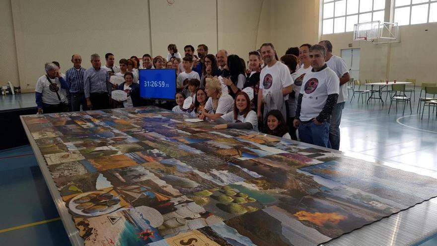 Algunos de los participantes en el montaje del puzle, hoy, junto al mural y el cronómetro con el tiempo en el que se logró la hazaña.