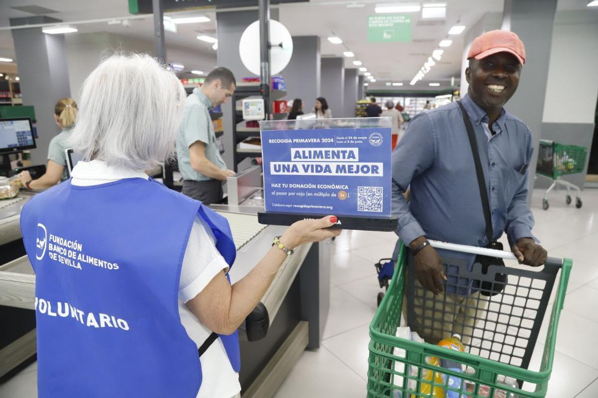 Una voluntaria del Banco de Alimentos sosteniendo un separador promocional de la recogida, junto a un cliente, en un supermercado.