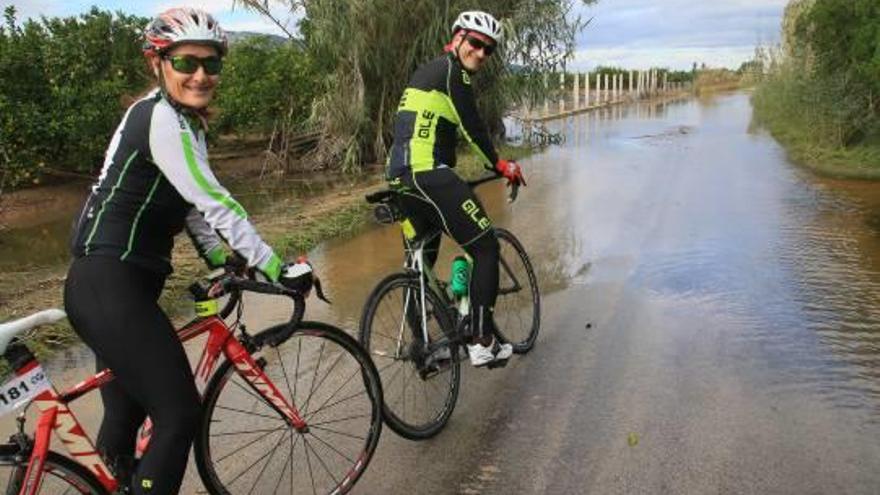 Dos ciclistas valoran si cruzan el camino inundado situado entre Xeraco y Tavernes.