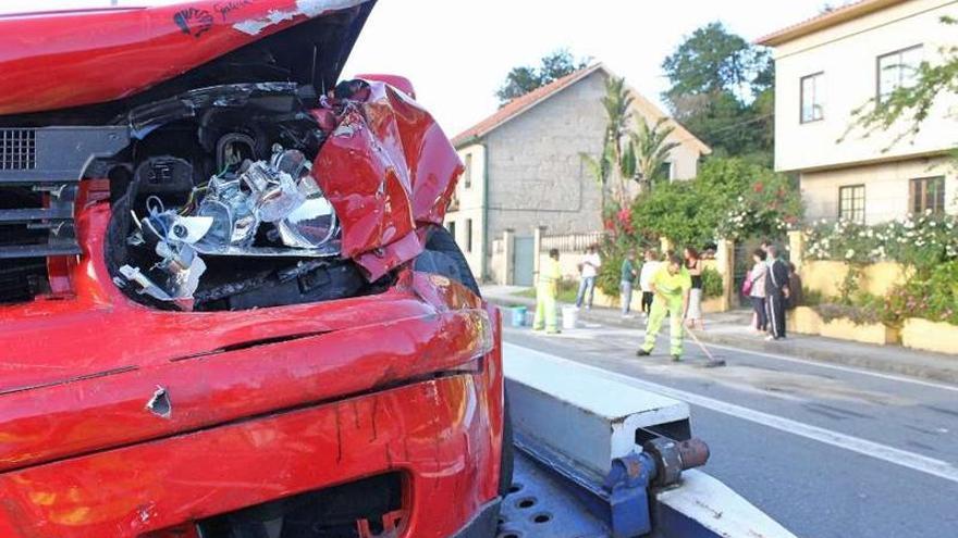 Operarios limpian la zona del accidente con uno de los vehículos implicados ya en la grúa.