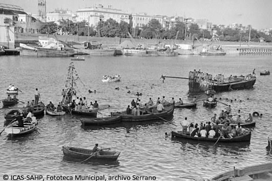 Embarcaciones alrededor de la barcaza de la cucaña, al fondo el Muelle de la Sal con su actividad portuaria. (1964)