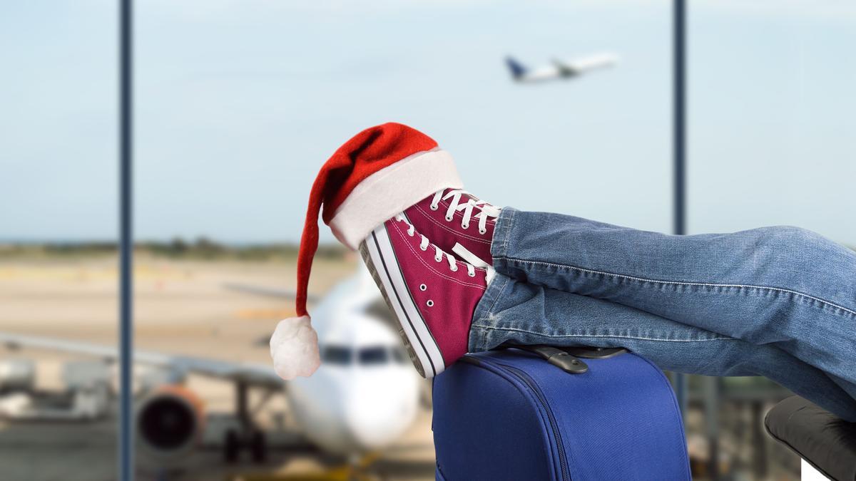 Muchacho joven con las piernas más de la maleta esperando en el aeropuerto con el sombrero de santa en los pies