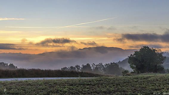 A punta de dia. El verd del camp i el bosc contrastava amb la boira baixa de la vall i el cel serè amb la llum del dia puntejant.