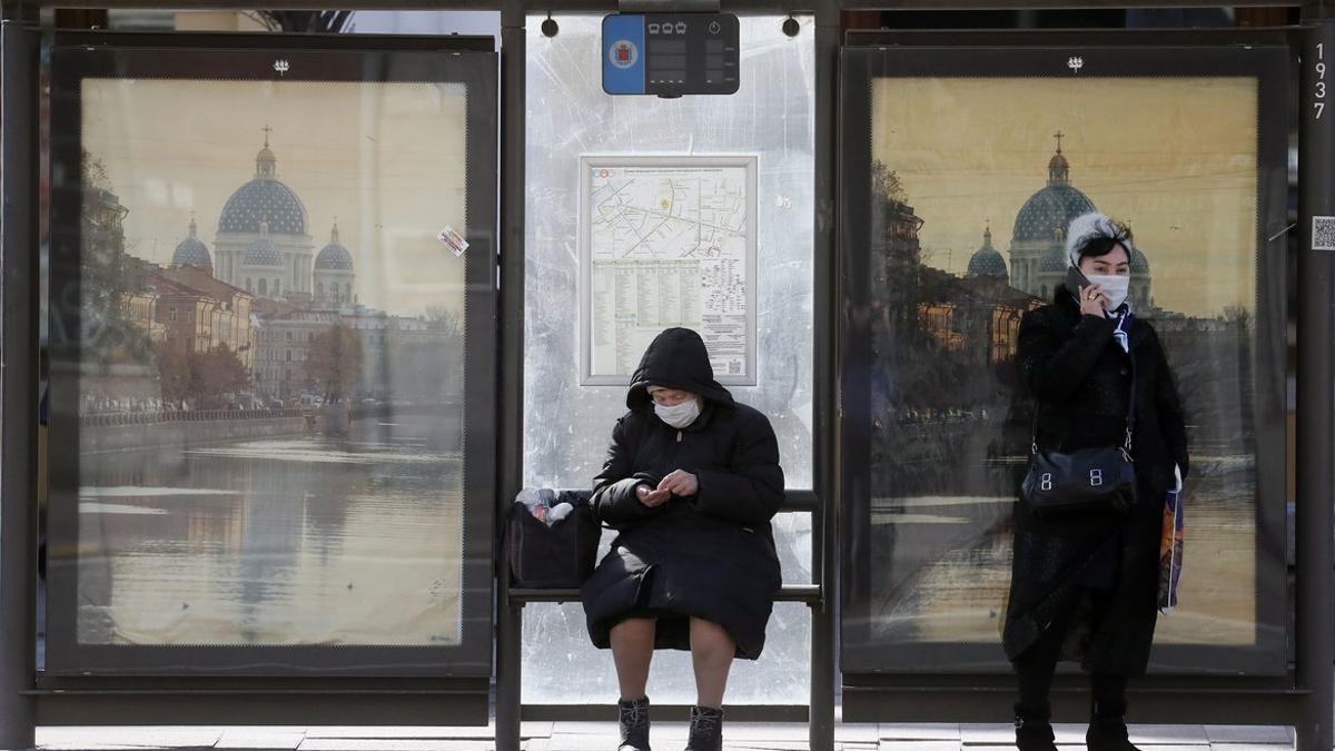 Unas mujeres con mascarillas en una parada de bus en San Petersburgo,