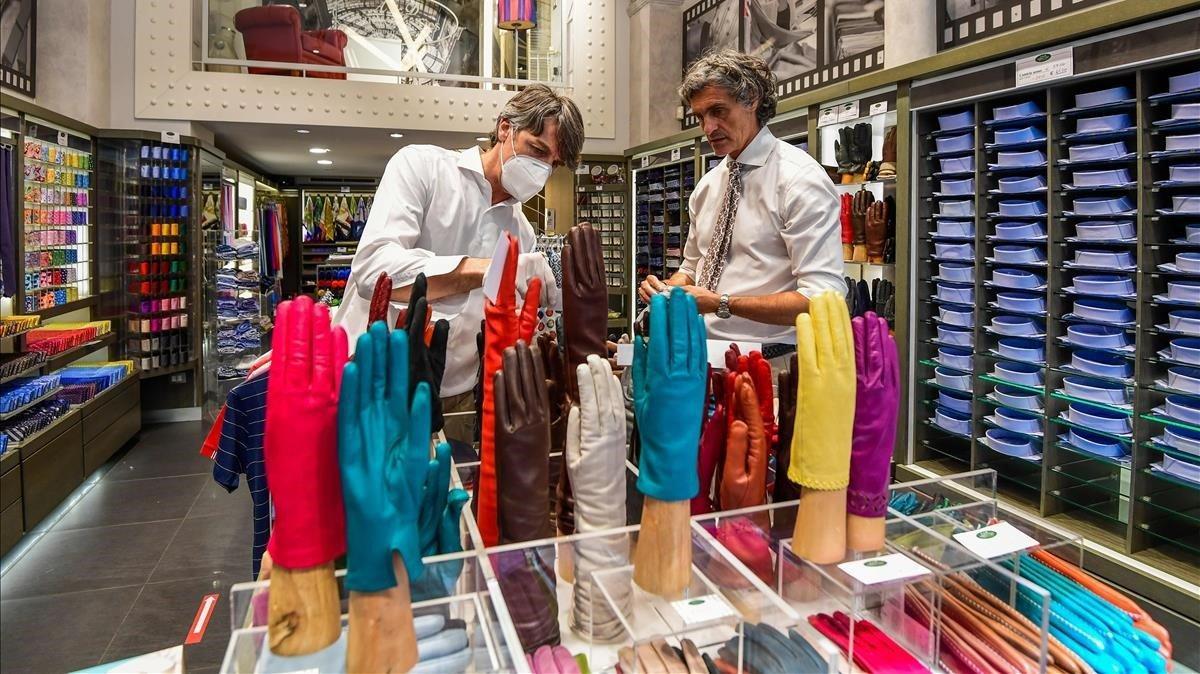Los vendedores organizan artículos en una tienda de camisas y corbatas para su reapertura en el distrito de la moda de Milán.