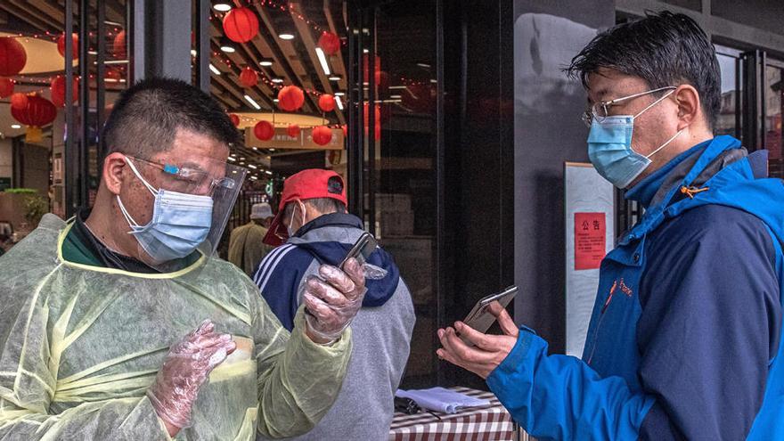 Un trabajador en traje de protección comprueba los códigos QR de salud de un hombre a la entrada de un centro comercial en Wuhan.