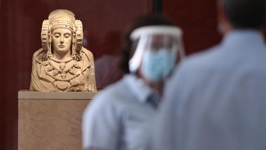 Dos trabajadores protegidos con mascarilla y pantalla vigilan una de las salas donde se encuentra la escultura de La Dama de Elche en el Museo Arqueológico