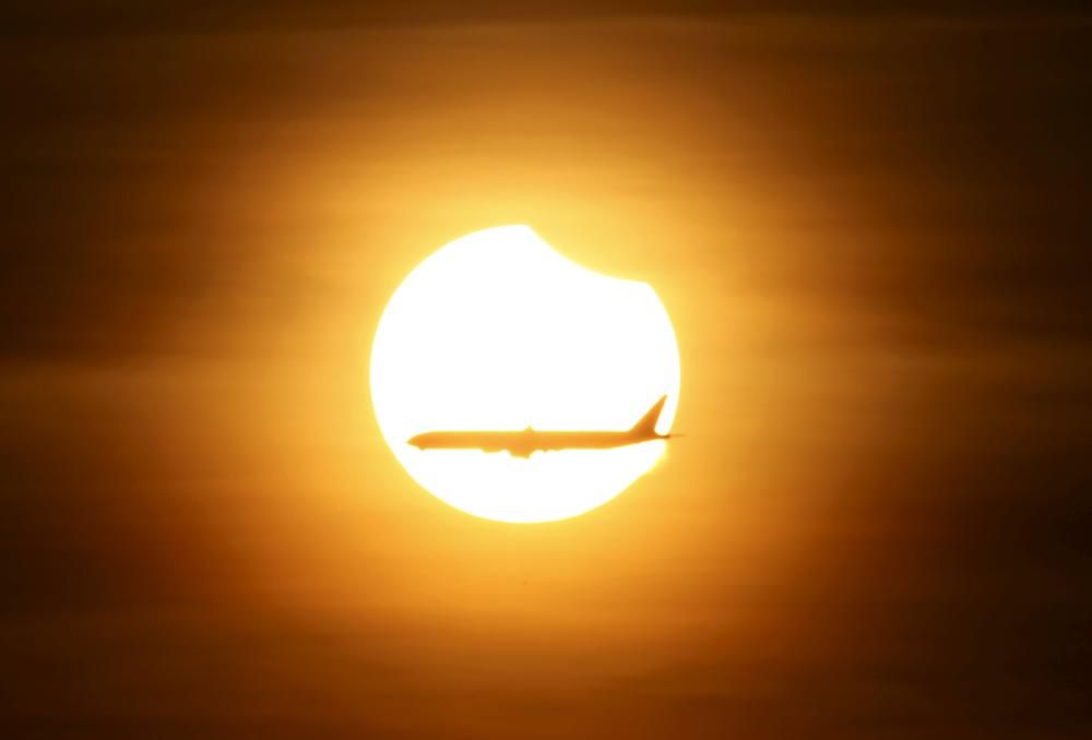 An aeroplane flies past the sun as it goes into ...