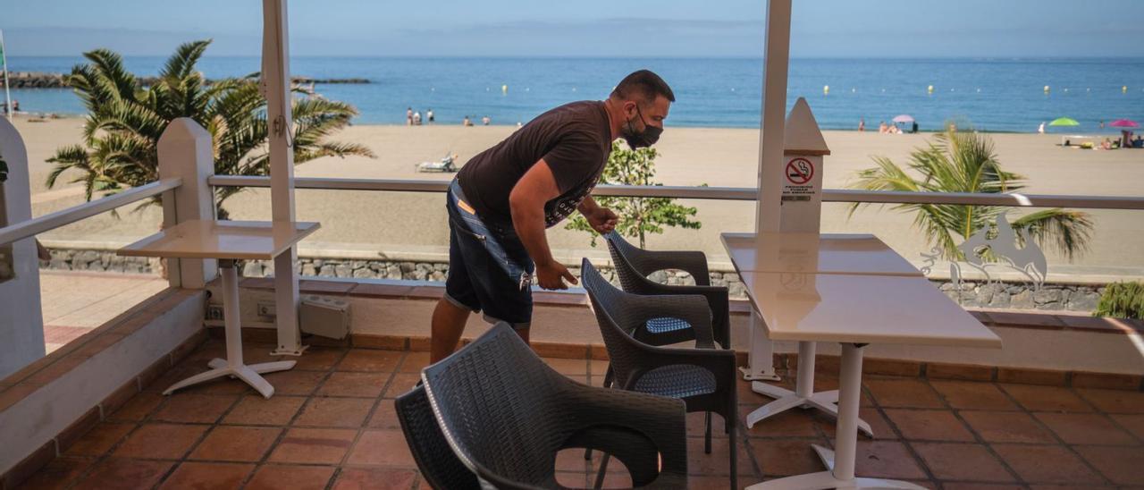 Un trabajador recoge las mesas de una terraza en el paseo de la playa de Los Cristianos, en el sur de Tenerife. | | ANDRÉS GUTIÉRREZ